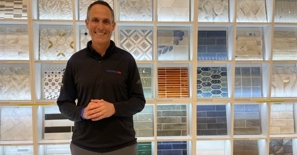 Scott Erlbaum stands in front of a colorful wall of tiles, showcasing various patterns and designs.