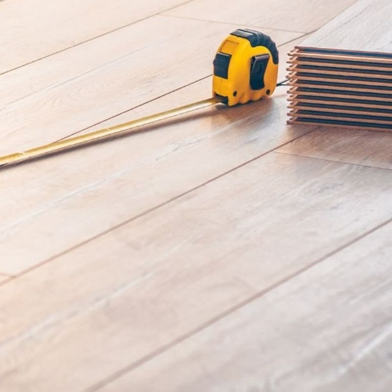 A yellow tape measure rests on a wooden floor, showcasing its length and flexibility.