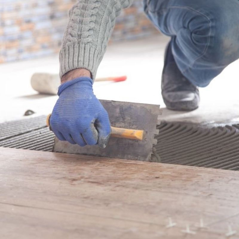 A man kneels on the floor, carefully laying tiles in a geometric pattern with tools nearby.