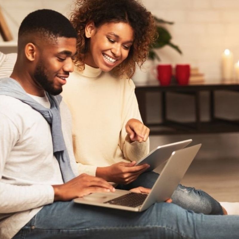 A young couple sits together on a couch, using a laptop in their cozy living room.
