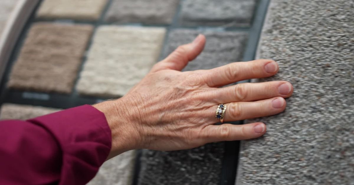 A hand reaching out to feel the texture of a carpet sample displayed on a surface.