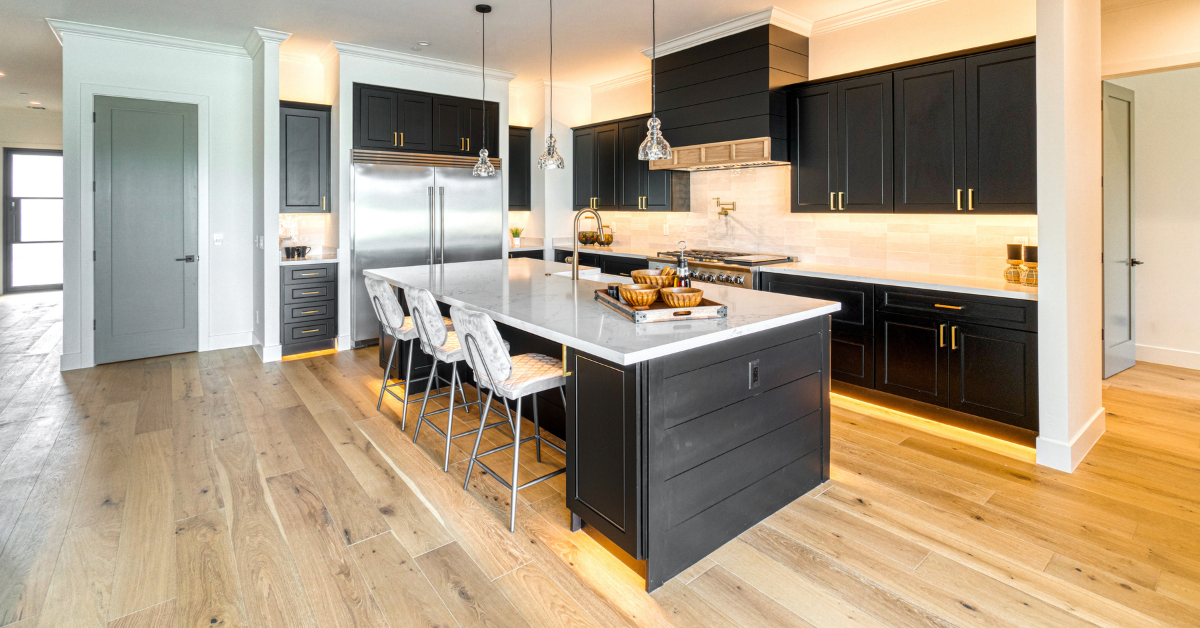 A modern kitchen featuring sleek black cabinets paired with bright white countertops & bright hardwood.