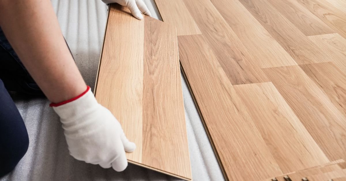 A person installing wooden flooring, carefully laying down planks in a well-lit room.