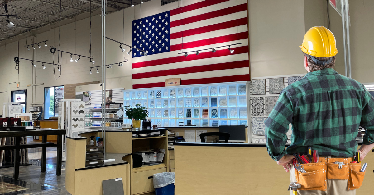 A man wearing a hard hat poses in front of a large American flag, representing dedication and national pride.