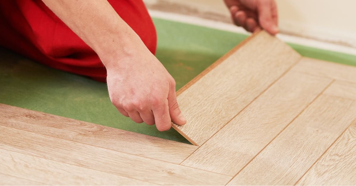 A person laying down wood flooring with another individual in red pants observing the process.