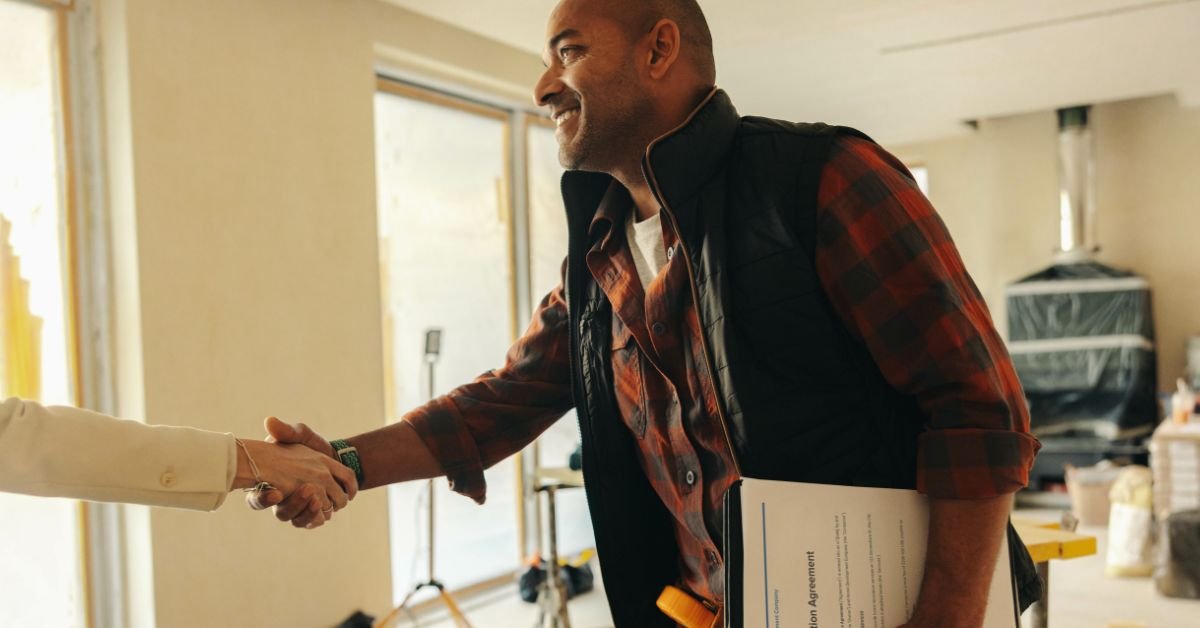 a man and woman shaking hands inside a cozy home, symbolizing agreement or partnership.