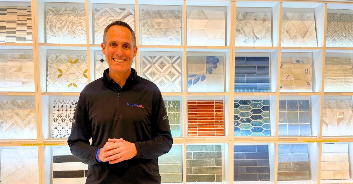 Scott Erlbaum stands in front of a colorful wall of tiles, showcasing various patterns and designs.