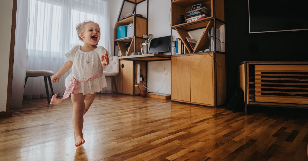 A little girl joyfully running across a brightly lit room, her hair flowing behind her.
